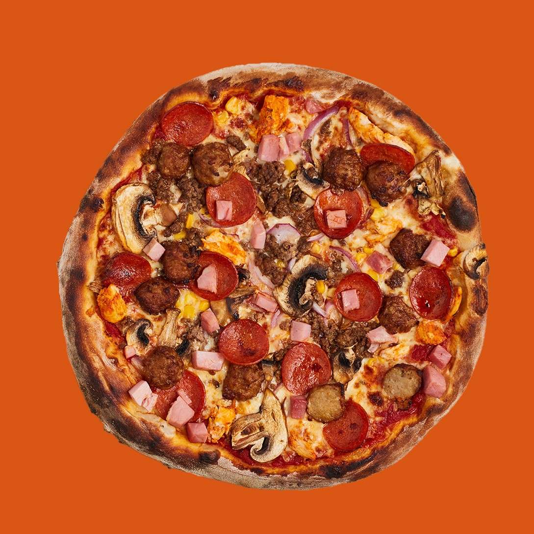 A fully loaded pizza rests flat, topped with pepperoni, sausage, ham cubes, mushrooms, onions, ground meat, cheese, and tomato sauce, against a solid orange background.