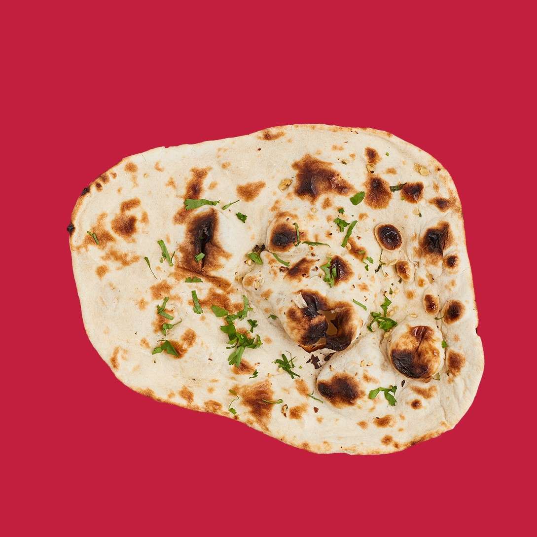 Flatbread rests, charred and sprinkled with chopped herbs, showing blistered spots and uneven edges, on a solid red background.