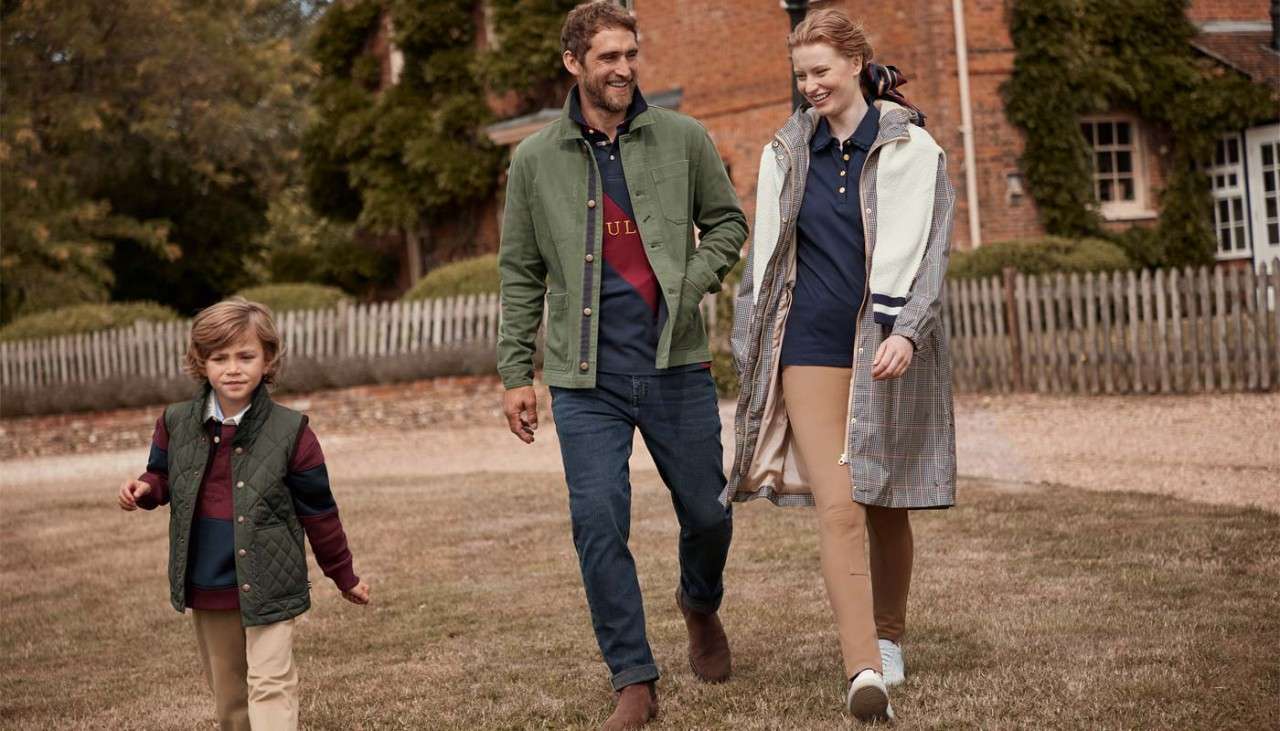 Family walking across a garden wearing Joules clothing.