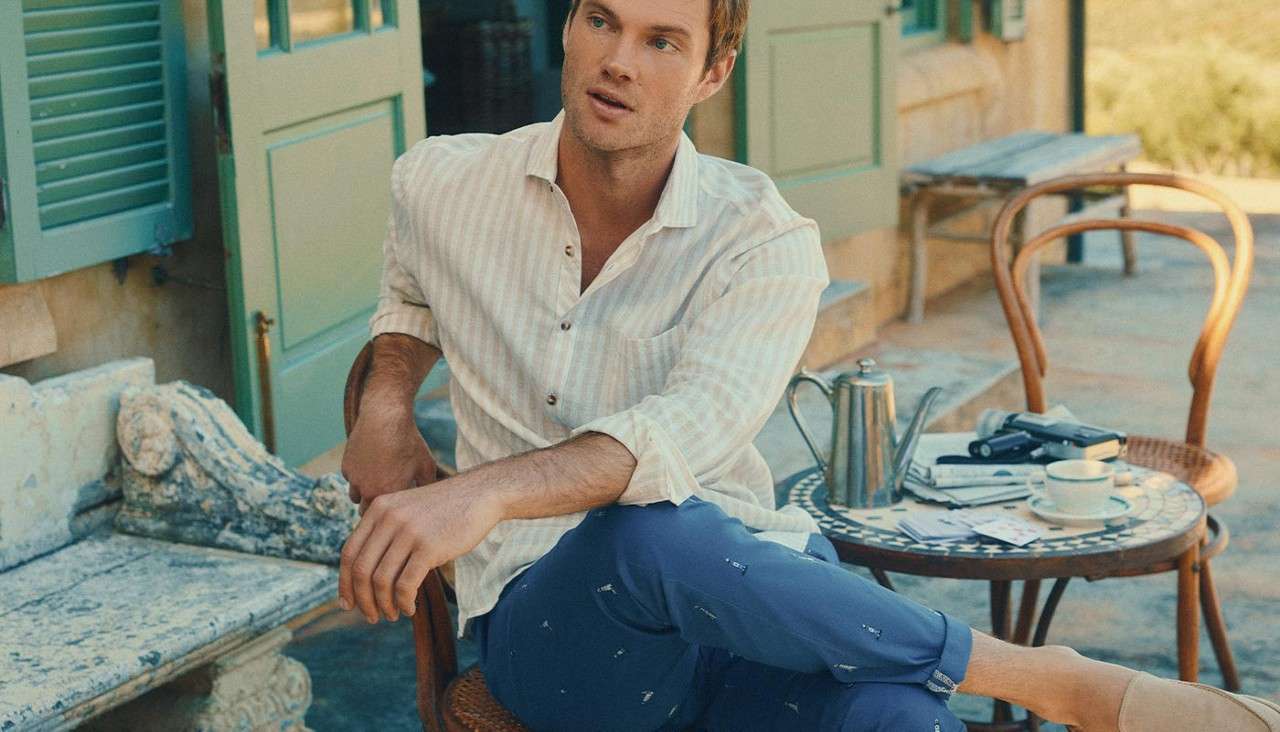 Man wearing cropped trousers with embroidered details and a button down shirt. 