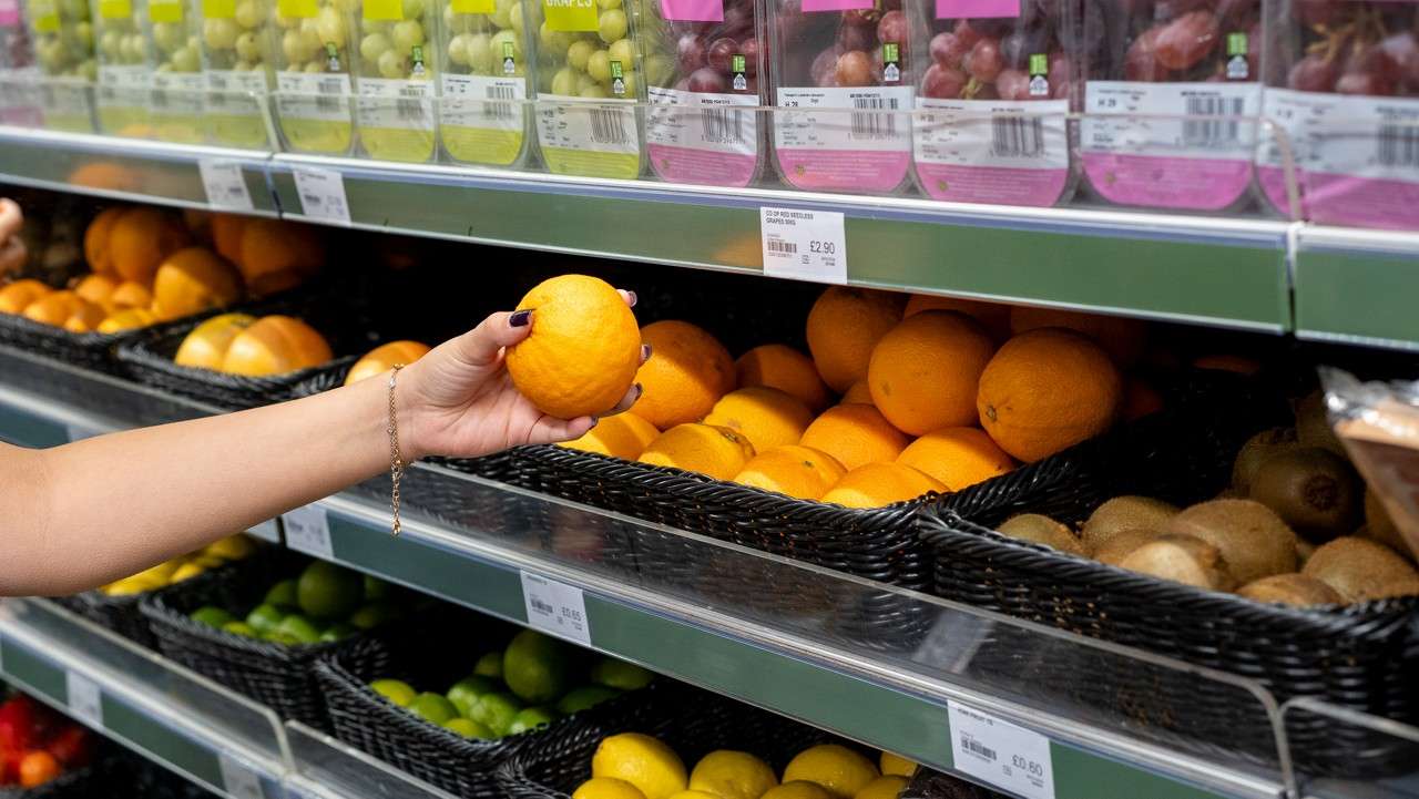 a hand picking up a orange from a shelf in parc market store