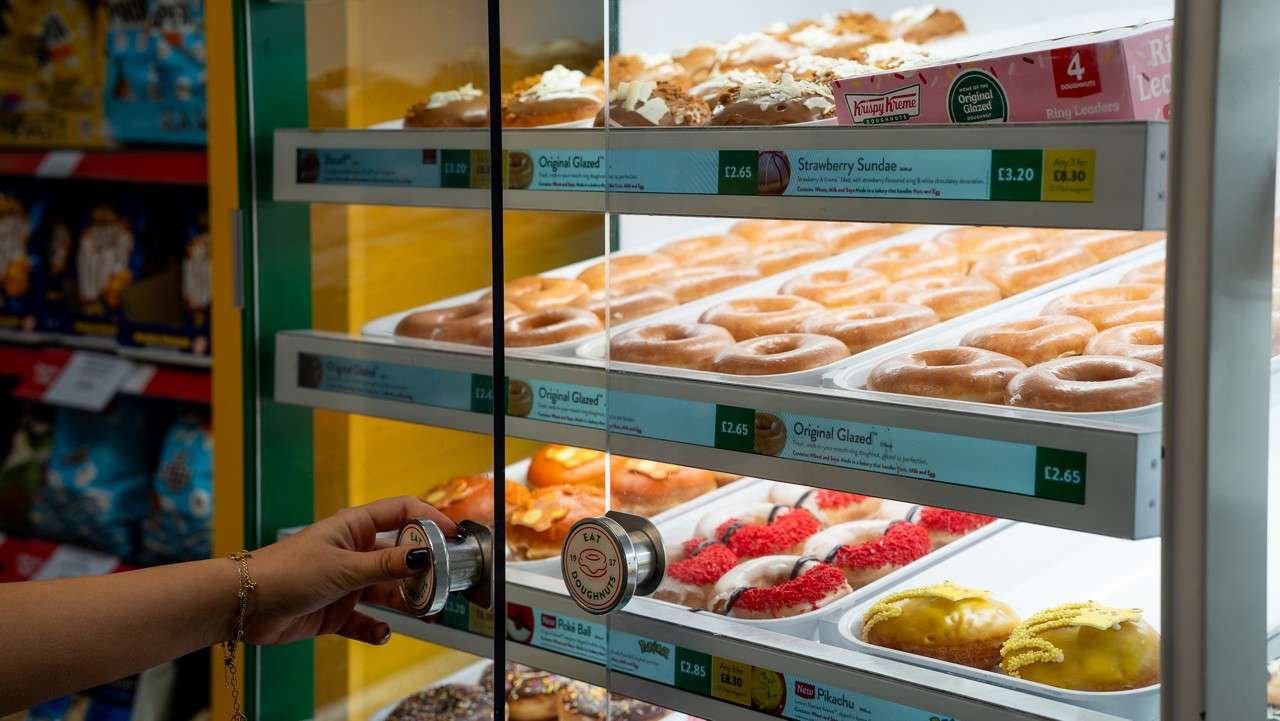 a hand opening a glass door to a selection of donuts on shelves