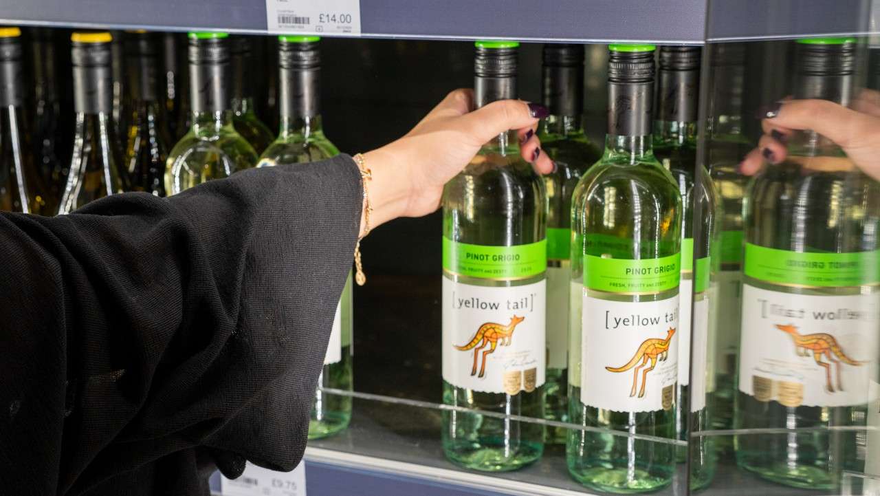 a hand picking up a bottle of white wine off a shelf