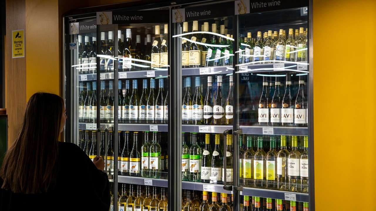 a women in a black jumper stood in front of shelves with bottles of wine
