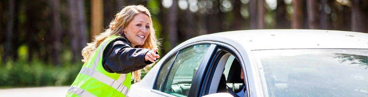 A woman wearing a hi-vis jacket directing a car to a parking space.