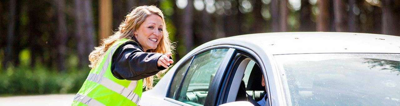 A woman wearing a hi-vis jacket directing a car to a parking space.