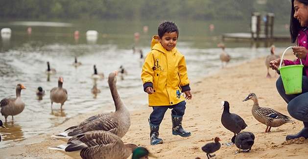 Young boy in a rain mac with his dinosaur umbrella