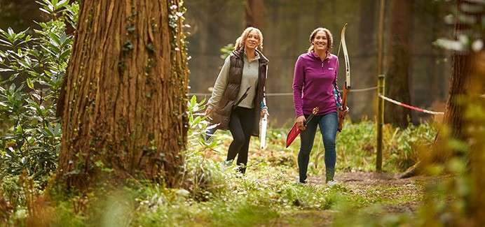 A mother and daughter doing Archery in the forest.