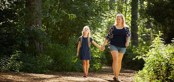A mother and daughter walk through the sunny forest 