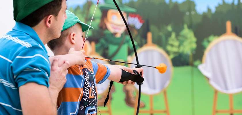 A father helping his son use a bow to aim at a target in the Little Outlaws activity.