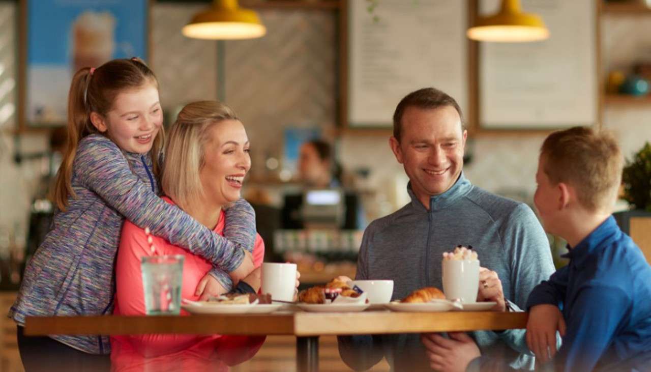 A family of four laughing and enjoying hot drinks in the Coffee House.