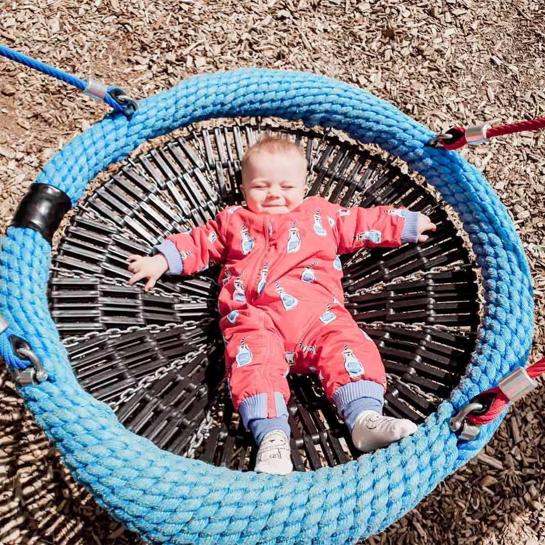 Baby laid in a round swing in an outdoor play area