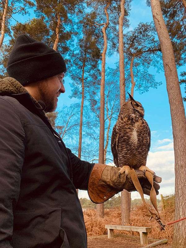 A man holding an owl in the forest.