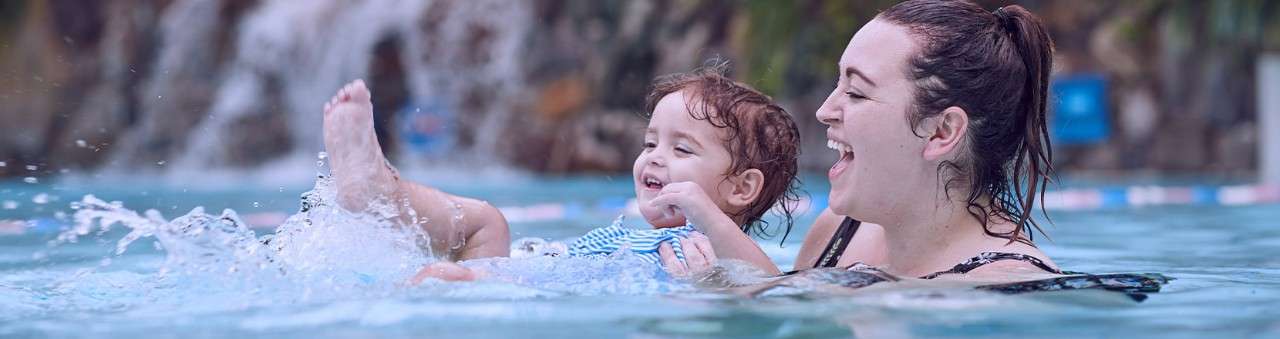 A mother and her small daughter splashing in the pool.