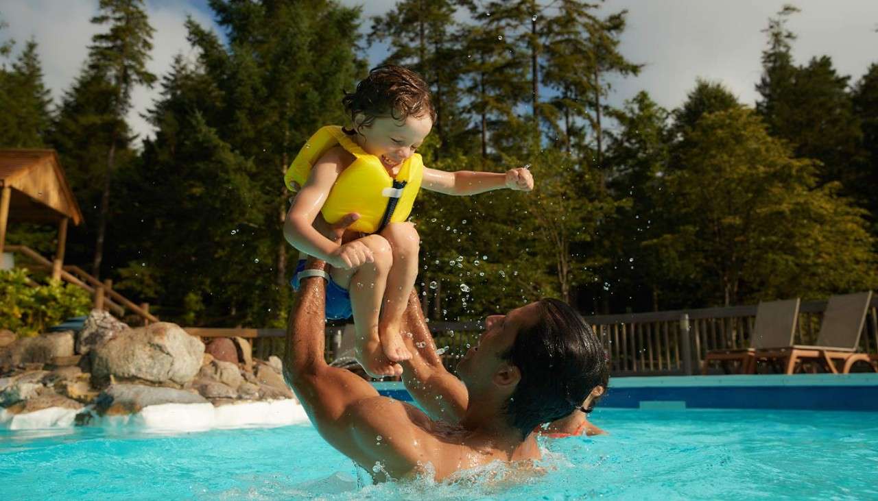 A father and child playing in the pool.