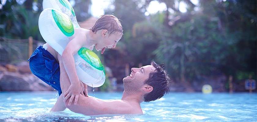 A father playing with his son wearing an inflatable pool ring in the Subtropical Swimming Paradise.
