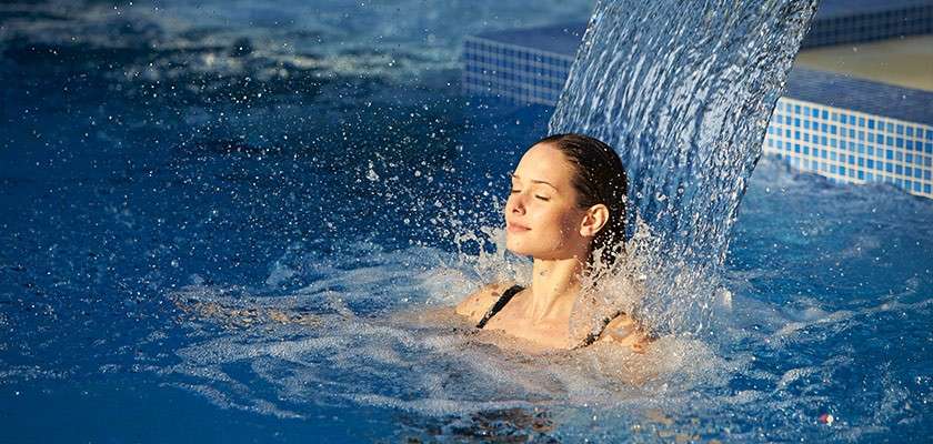 A woman in a pool relaxing under a water jet. 