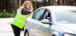 A woman in a hi vis jacket directing a car to a parking space