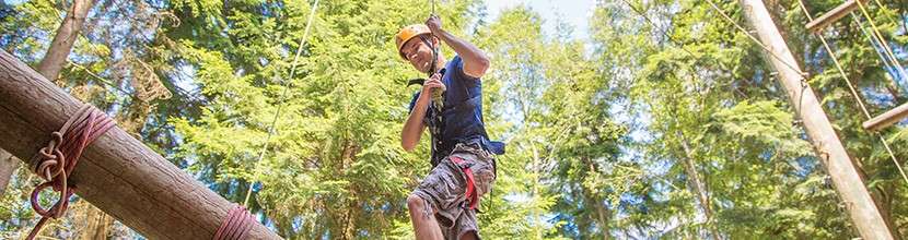 A man walking along a log in the trees in the Aerial Adventure course