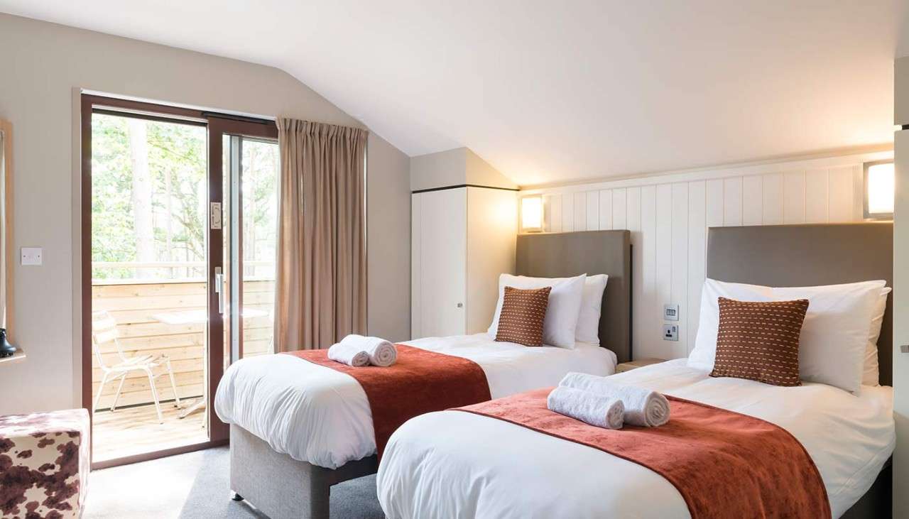 A twin bedroom inside a lodge with two neatly made beds and sun shining through the window
