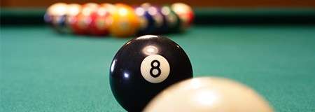 Eight ball rests near the cue ball, sharply focused in the foreground; racked colorful balls blur in the distance on a green felt pool table. Text: 8.