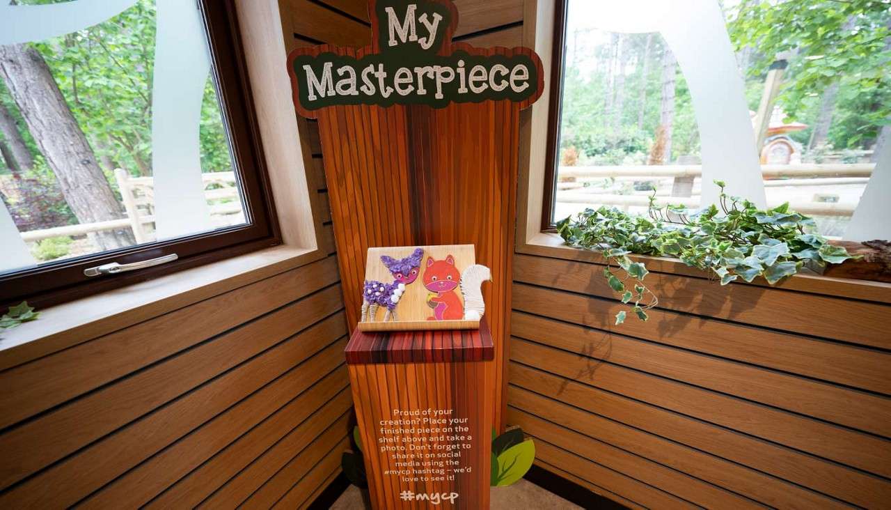 Wooden display stand showcases a child’s artwork between two windows. Text: “My Masterpiece. Proud of your creation? Place your finished piece on the shelf above and take a photo. Don’t forget to share it on social media using the #mycp hashtag - we’d love to see it! #mycp.”