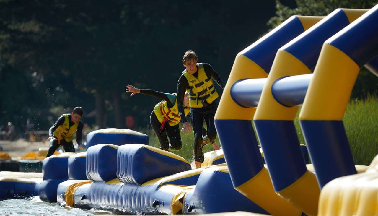 People walking over an inflatable obstacle course on the lake.