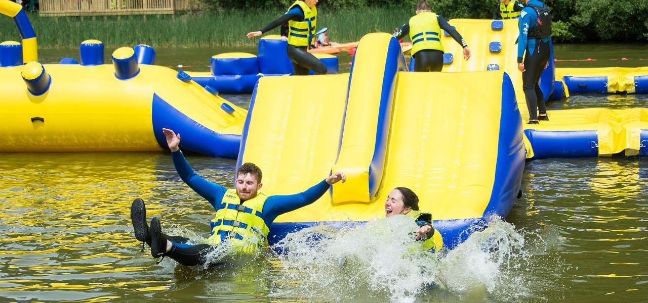 Couple sliding down an inflatable and making a splash in the lake.