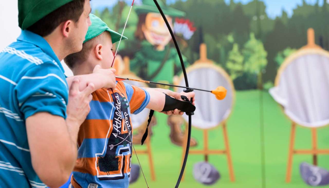 Young boy and an adult aiming a bow in Little Outlaws 