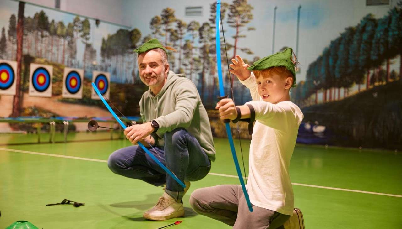 Young boy and an adult aiming a bow in Little Outlaws 