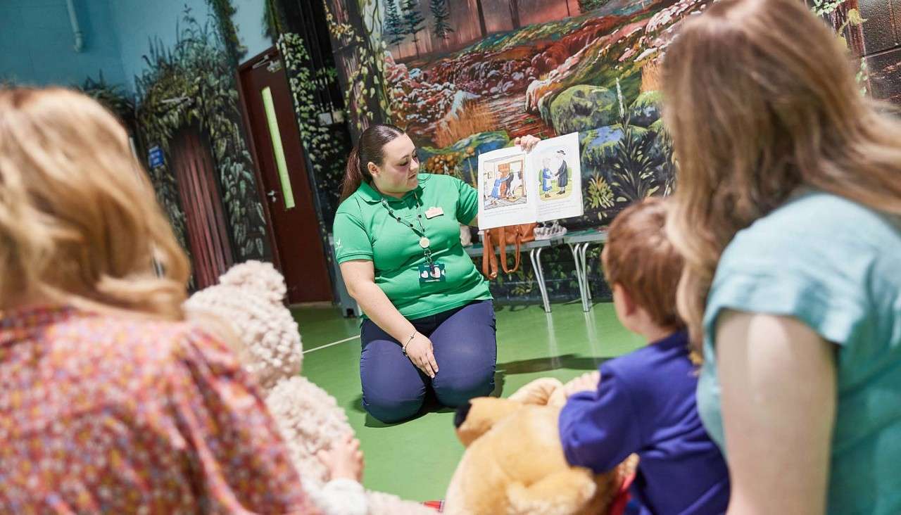 Staff member reading a story book to a group of young children.