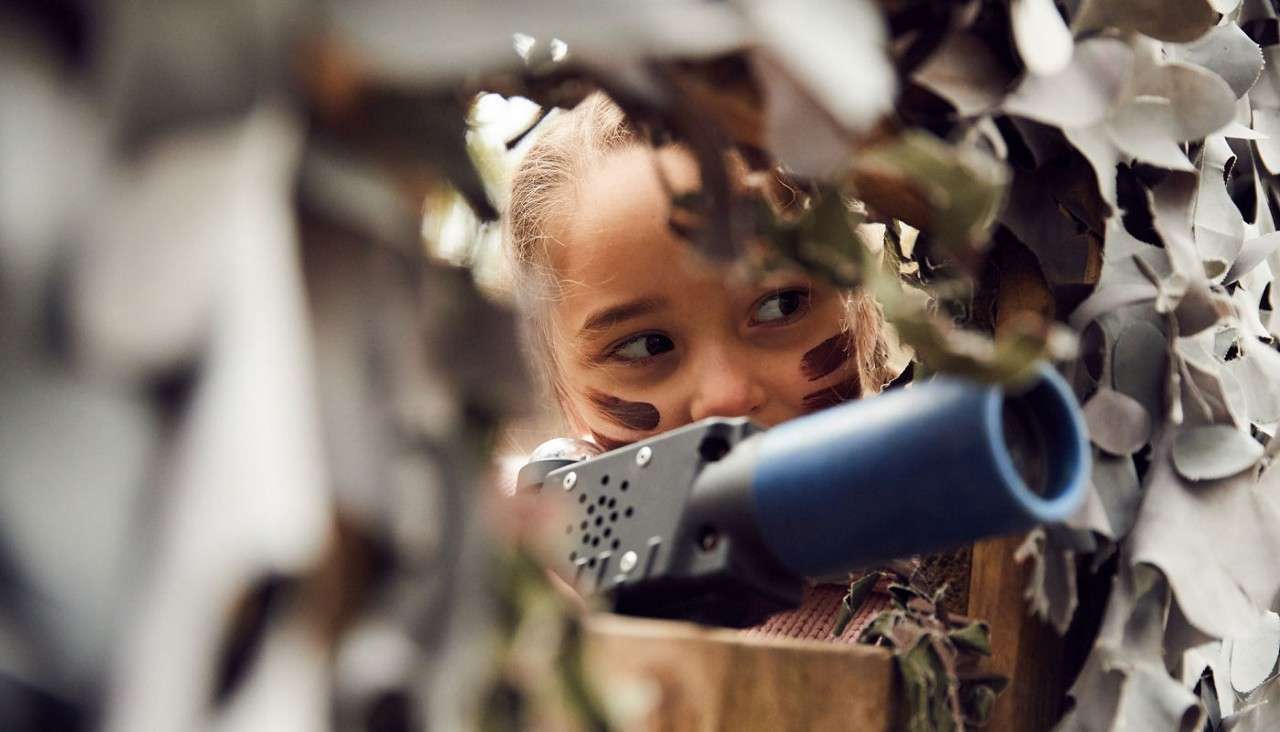 Young girl aiming a laser gun through a camouflage net