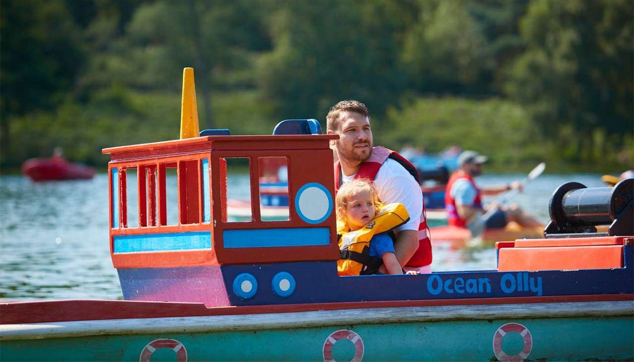 A man and young girl sailing a colourful boat on the lake.