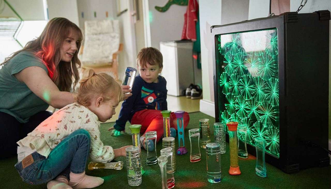 A woman with two young children exploring different glowing objects.