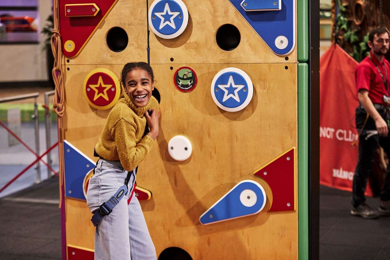 A teenager smiling at the camera ready to scale the climbing wall.