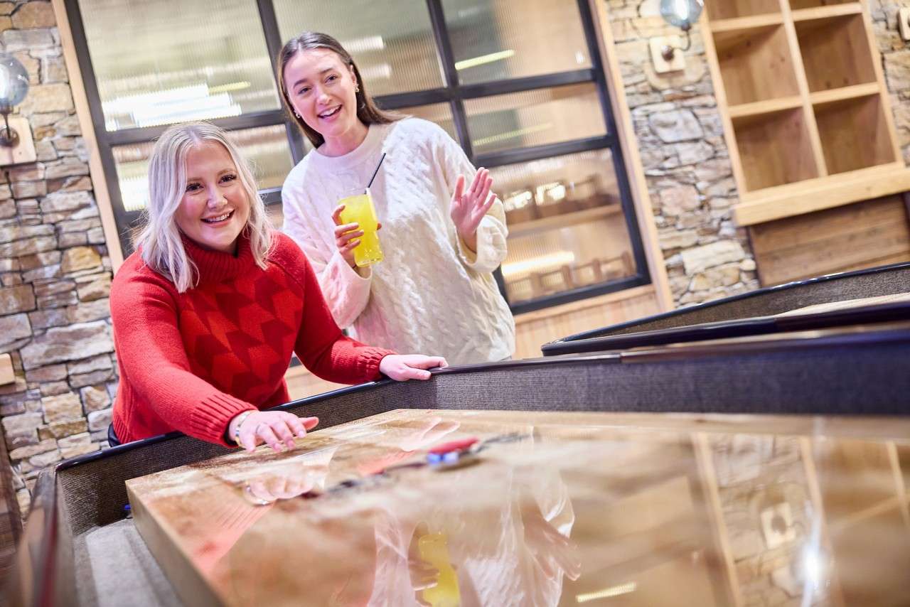Two ladies laughing on the shuffleboard table