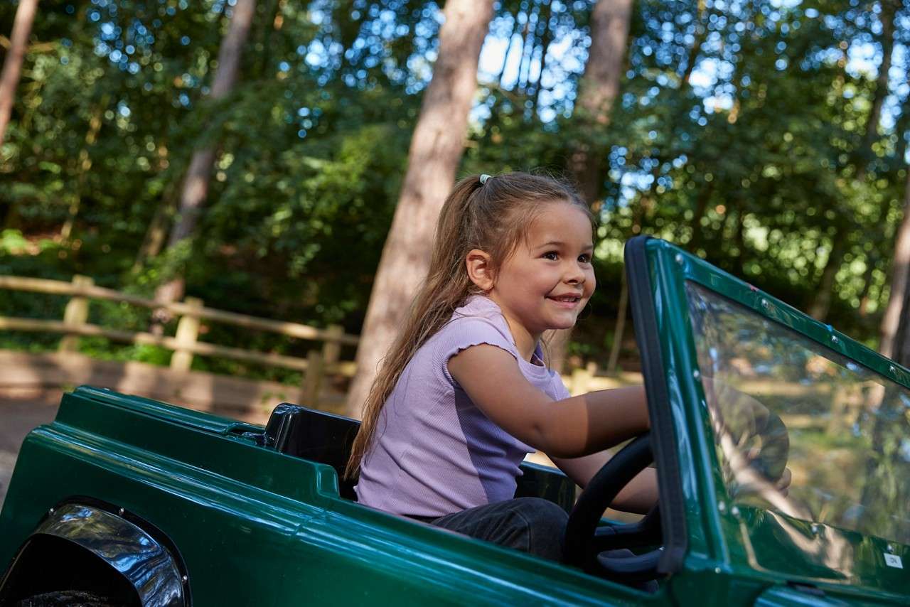 A close up of a girl smiling and holding the steering wheel.