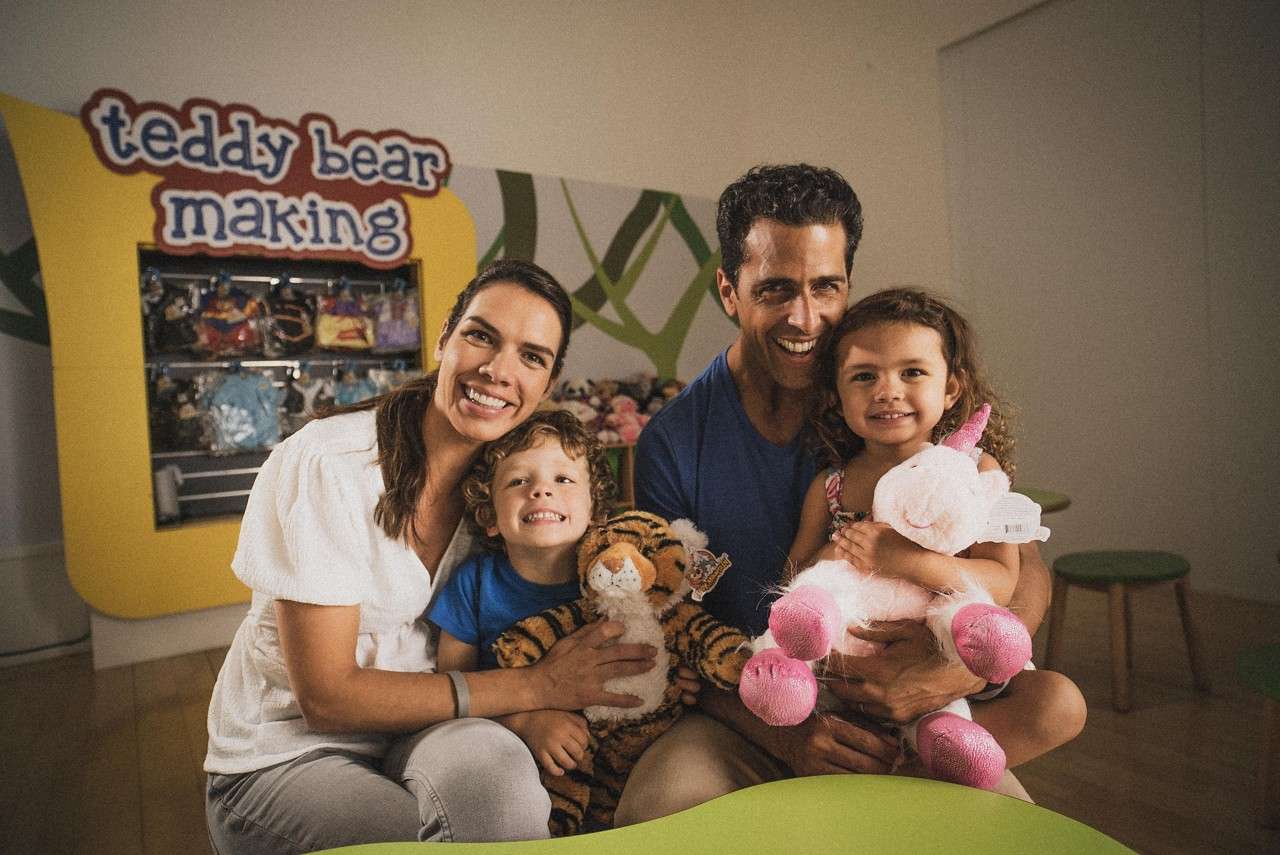 A family smiling at the camera holding their teddies. 