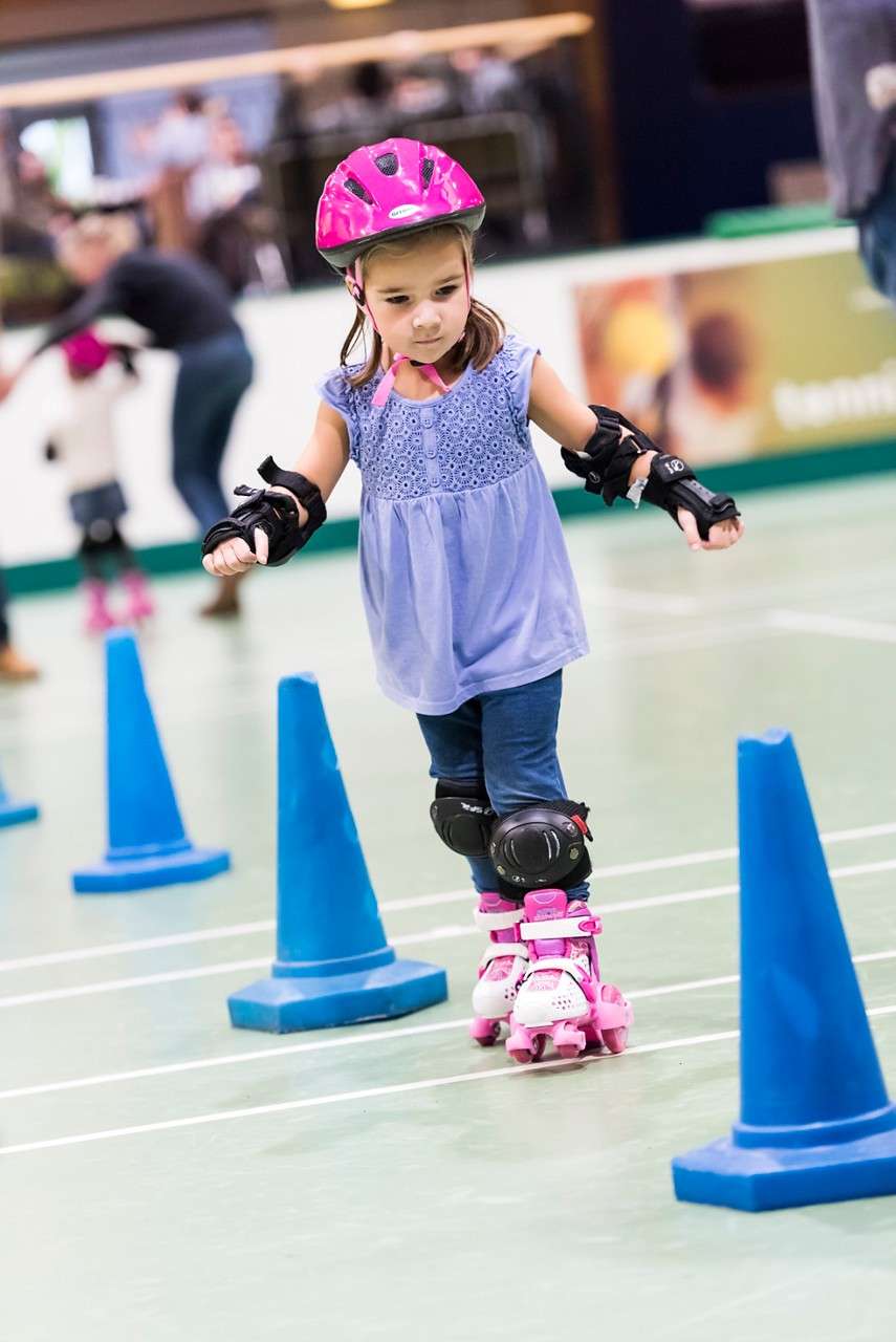 Young girl with a helmet and knee pads, roller skating around cones.