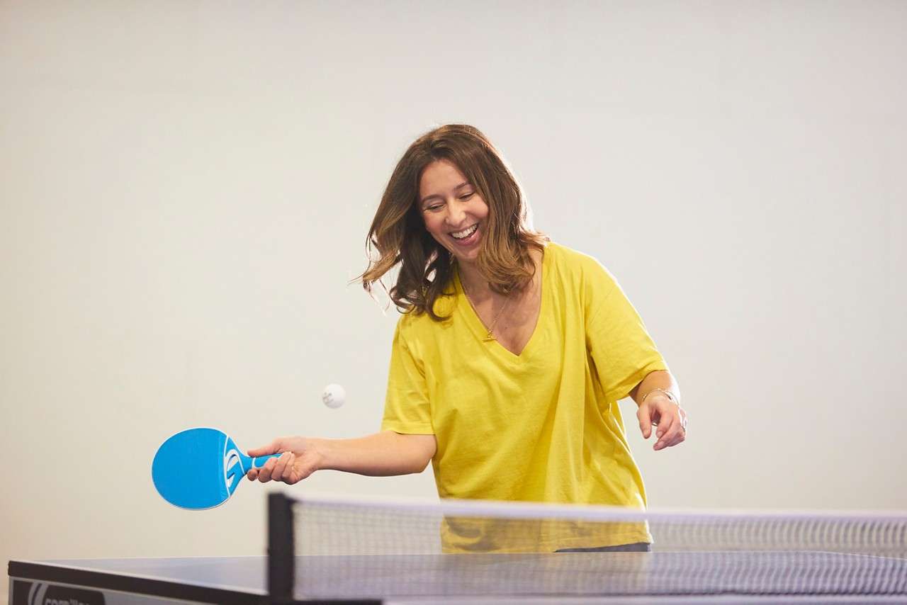 A lady laughing as she gets ready to hit the table tennis ball with her paddle