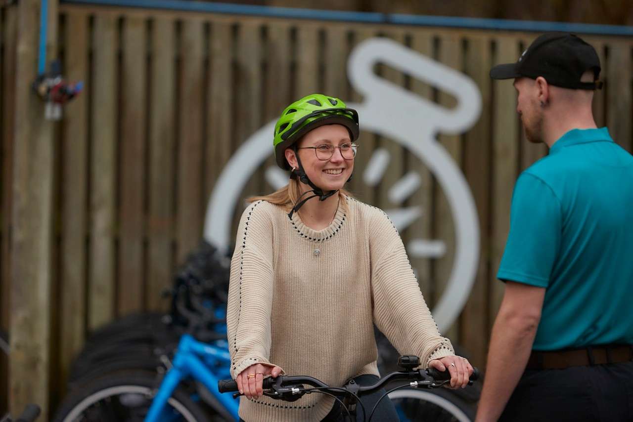 A girl smiling and stood with a cycle in the Cycle Centre, talking to a member of staff.