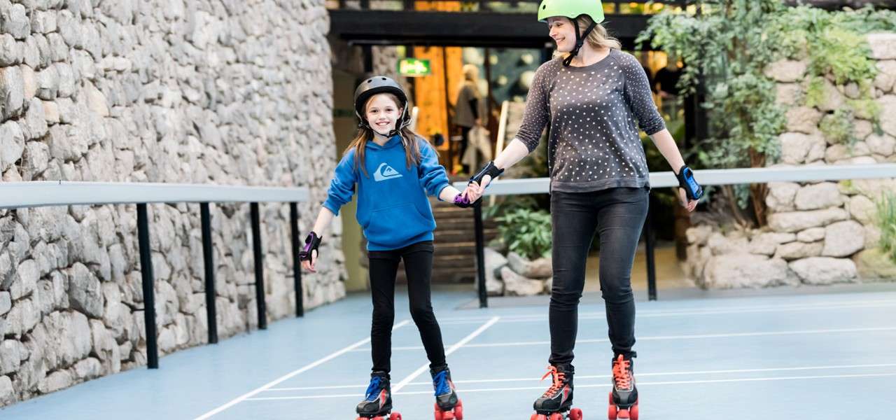 Woman and a young girl roller skating wearing helmets and knee pads.