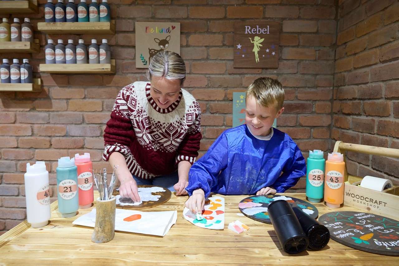 Two people painting wooden plaques.