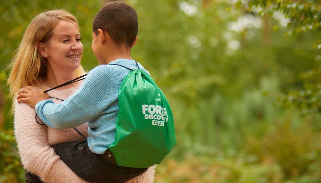 Woman carrying a small boy on a Forest Discovery Trail.