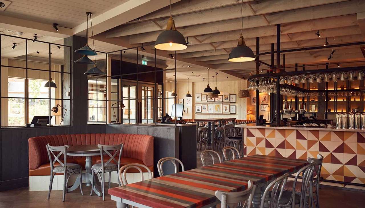 Long table for families, with industrial style lights overhead. The bar and a booth can be seen in the background