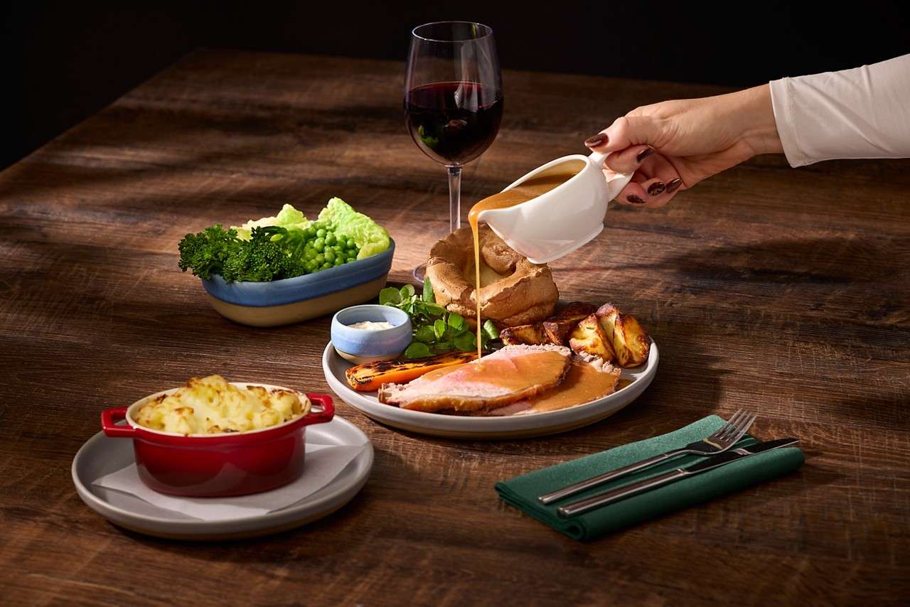 Roast dinner with sliced meat, seasonal vegetables and someone pouring gravy.