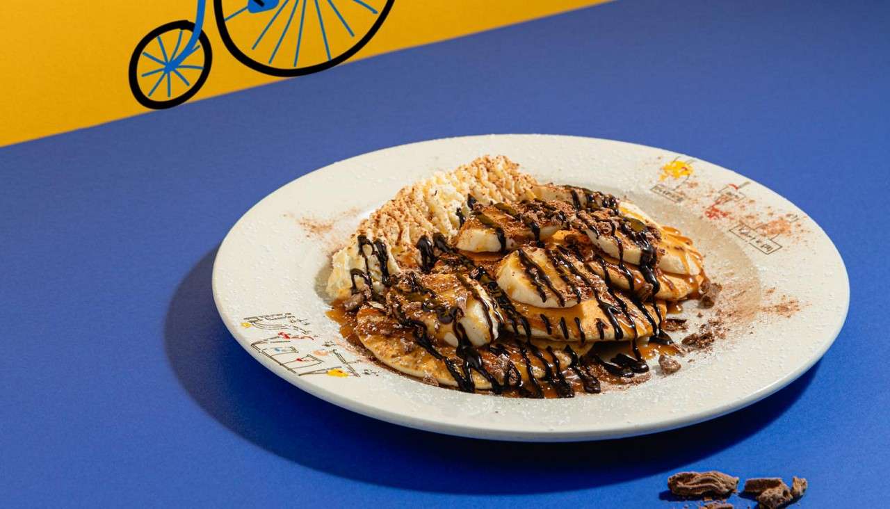 Pancakes topped with sliced banana, toffee and chocolate sauce, crushed Flake and fresh whipped cream.