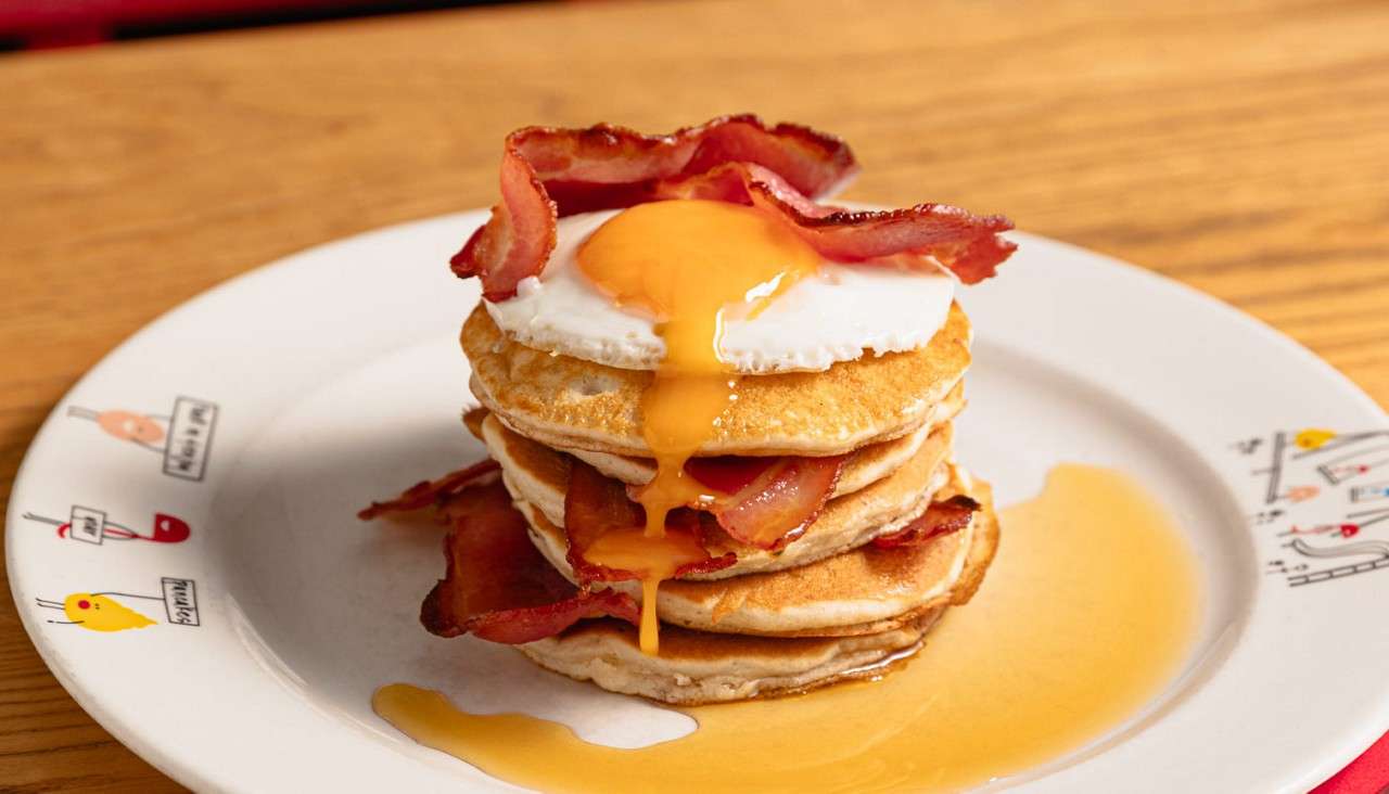Stacked pancakes topped with a runny egg and crispy bacon.