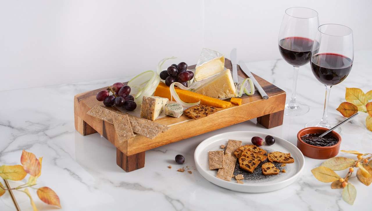 a wooden board on a table, with a selection of cheeses and two glasses of wine