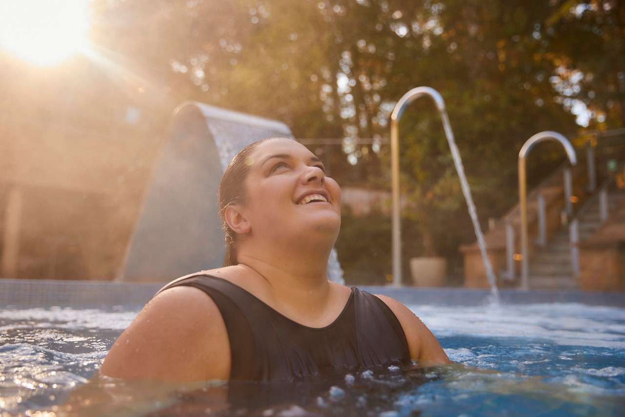 Women un a black swimsuit in a an outdoor pool surrounded by forest